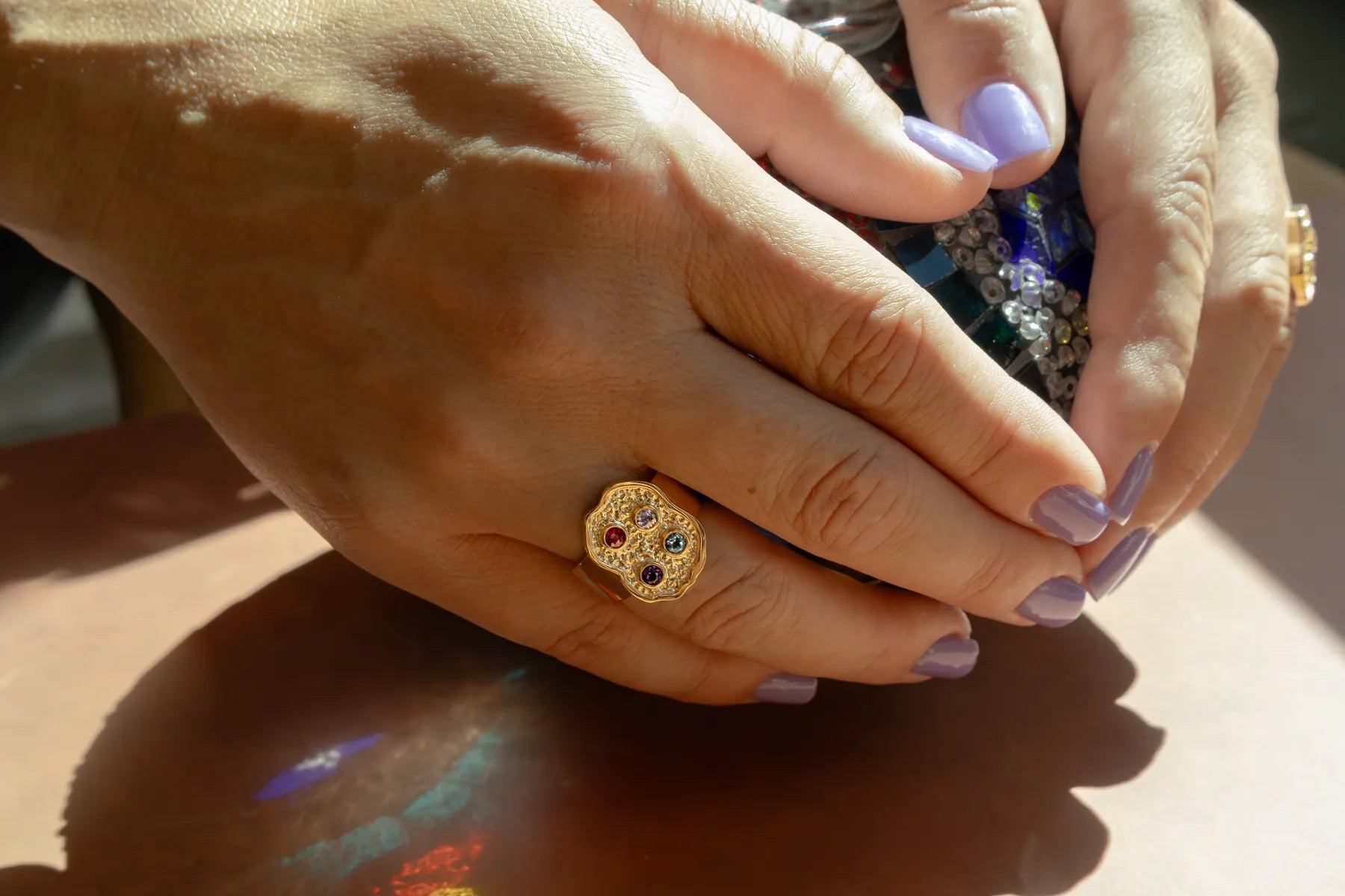 Two hands in the sun, each wearing a stone-set gold ring