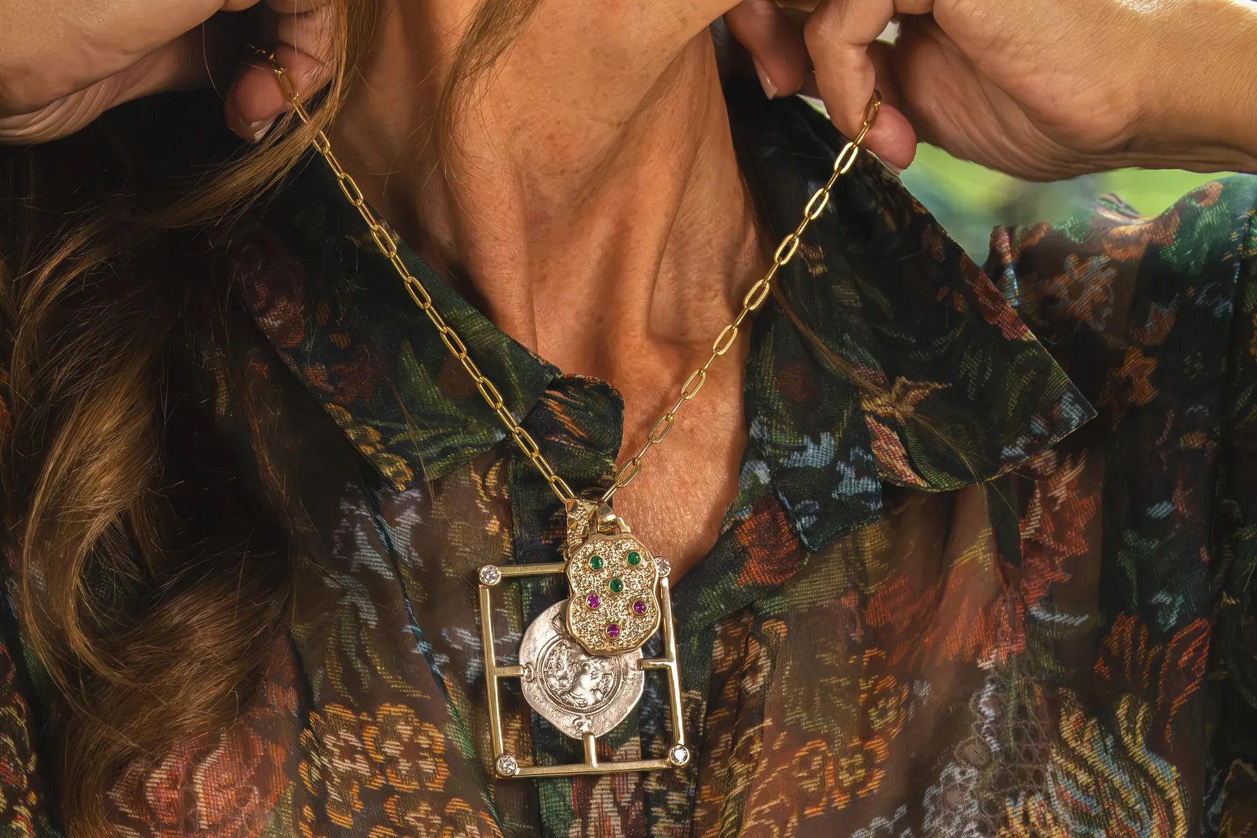 A gold pendant worn over a printed blouse