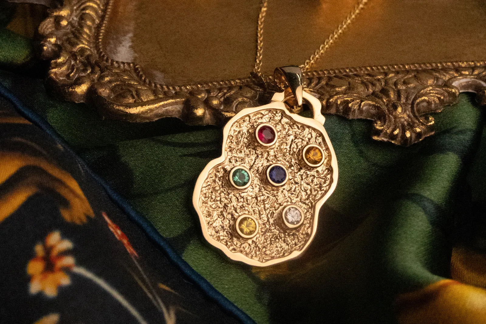 The Nugget Pendant in gold with multi-colour stones, photographed on printed green silk