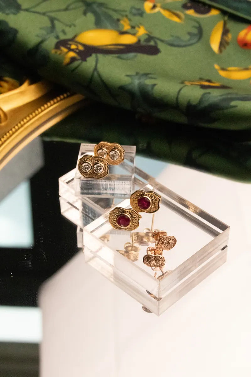 Ruby-set gold studs and a ring on clear acrylic blocks